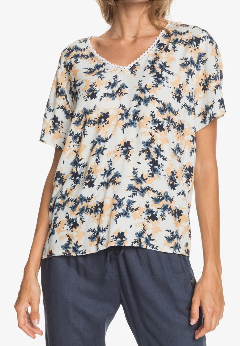 Blusa de manga corta con estampado floral y escote en V, que presenta un fondo crema con flores azules y durazno, y un borde de encaje alrededor del escote.