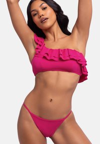 Ružičasti bikini set s volanima na jednom ramenu i minimalističkim donjim dijelom; glatka tekstura, usklađen dizajn i živahna boja.
