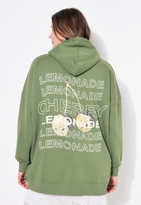 Sudadera verde de gran tamaño con capucha ajustable. Presenta texto blanco que dice "LEMONADE" y "CHERRY", junto con gráficos de bola de discoteca.