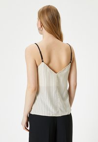 Camisón de satén en crema con lunares negros, con tirantes finos ajustables y un diseño de espalda en forma de V profunda. Textura suave, corte relajado.