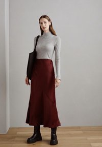 Top cu guler înalt cu dungi, asortat cu o fustă de satin burgundă cu cusături diagonale, purtat cu cizme negre cu platformă și o geantă de umăr neagră.