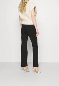 Kortemouwen, geribbelde crème trui, gecombineerd met zwarte, op maat gemaakte broek en beige hoge hakken. Soepele texturen en moderne snit.