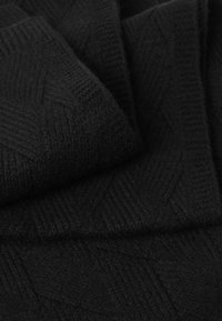 Tissu noir tricoté avec un motif en chevrons texturé. Le matériau semble doux et chaud, mettant en valeur des épaisseurs de fil variées.