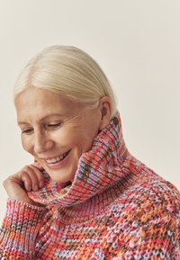 Mitmevärviline kootud kampsun kõrge kraega, kus on roosa, oranži ja pruunide toonide segu ning tekstureeritud disain.