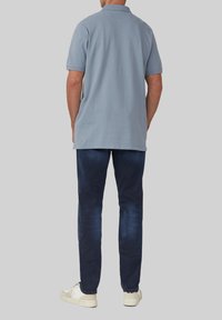 Himmelblaues Poloshirt mit umgeschlagenem Kragen, kombiniert mit dunkelblauen Jeans und weißen Sneakers, von hinten betrachtet.