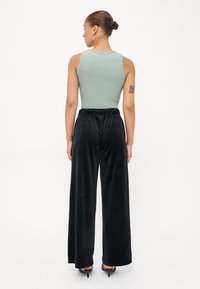 Lys grøn ribbet tanktop kombinert med løse svarte sammetbukser. Buksene har elastisk liv for komfort og en flytende, hel lengde design.