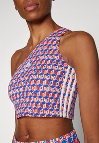 En axel crop-top med ett färgglatt hexagonalt mönster, i röda, blå och vita nyanser, med tre vita ränder på ena sidan.