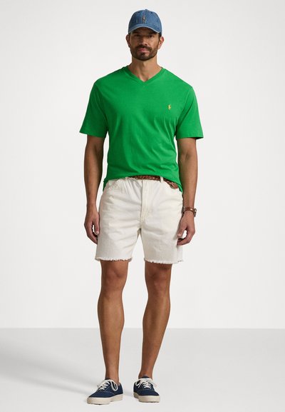 Zaļš īsām piedurknēm V veida kakla krekls, balti denim šorti ar plēstām malām un zilas kedas, papildināti ar gaiši zilu cepuri.