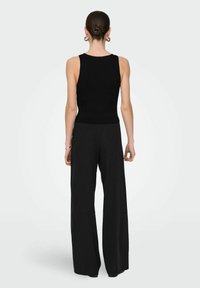 Débardeur noir côtelé avec une coupe courte et un ourlet festonné, associé à un pantalon noir taille haute à jambes larges pour une silhouette affinée.