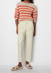 Randig stickad tröja i orange och beige, matchad med ljusbeiga tapered byxor och krämfärgade sandaler med korsade remmar.