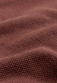 Gros plan d'un tissu texturé avec un motif de tricot dense et petit dans une couleur mauve atténuée, montrant des plis doux et une surface douce.