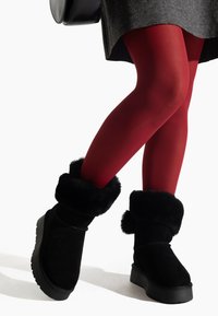 Botines de ante negros con un grueso puño forrado de piel y suela de goma, combinados con medias rojas y un vestido gris.