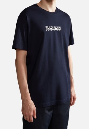 Mand iført en marineblå T-shirt med korte ærmer og "NAPAPIJRI geographic"-logoen centralt på brystet.