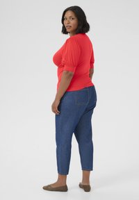 Rode getailleerde t-shirt met pofmouwen, gecombineerd met cropped blauwe jeans. De jeans hebben een klassieke denimtextuur en twee achterzakken.