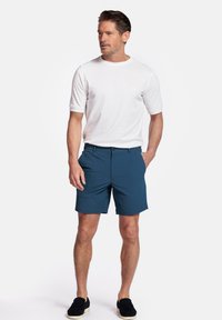 Witte korte mouwen t-shirt, marineblauwe shorts en zwarte instappers. Focus op casual streetwear, met een relaxed fit en een eenvoudig ontwerp.