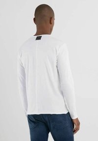 T-shirt bianco a maniche lunghe, con collo rotondo e un'etichetta nera sul retro. Tessuto morbido dalla texture liscia, vestibilità casual.