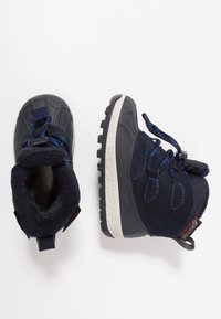 Granatowe zimowe buty z teksturowaną powierzchnią zewnętrzną, elastycznymi sznurowadłami, podszewką z sztucznego futra oraz czarną gumową podeszwą z wzorzystym bieżnikiem.