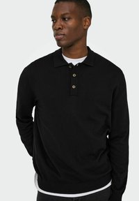 Melnā, garām piedurknēm, polo džemperis ar apkakli, trīs pogu vairojumu, ribota aproču daļu un apakšmalu. Mīksta tekstūra un piegulošs dizains.