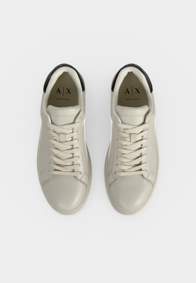 Двойка бели ниски маратонки Armani Exchange с черен детайл на петата и бели връзки, гледани отгоре на обикновен фон.