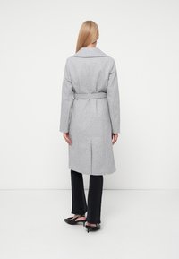 Siv coat iz volne z pasom, z odrezanimi klapami in dolžino pod koleni. Ima srednji zadnji razporek za udobno gibanje.