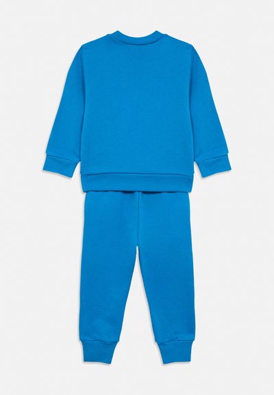 Ensemble sweat-shirt bleu à manches longues et pantalon assorti avec poignets côtelés, vu de dos sur fond blanc.