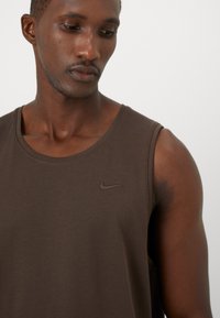 Brun Nike tank top med rund halsudskæring, der har en diskret broderet logo. Blødt, glat stof med en afslappet pasform.