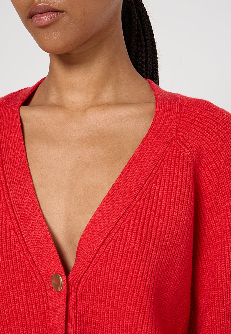 Roter gerippter Cardigan mit tiefem V-Ausschnitt und subtiler Textur, ausgestattet mit einem silbernen Knopfdetail vorne.