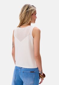 Witte mouwloze top met een gestructureerde, gebreide achterkant met een ruitpatroon. Gecombineerd met lichtblauwe denim jeans.