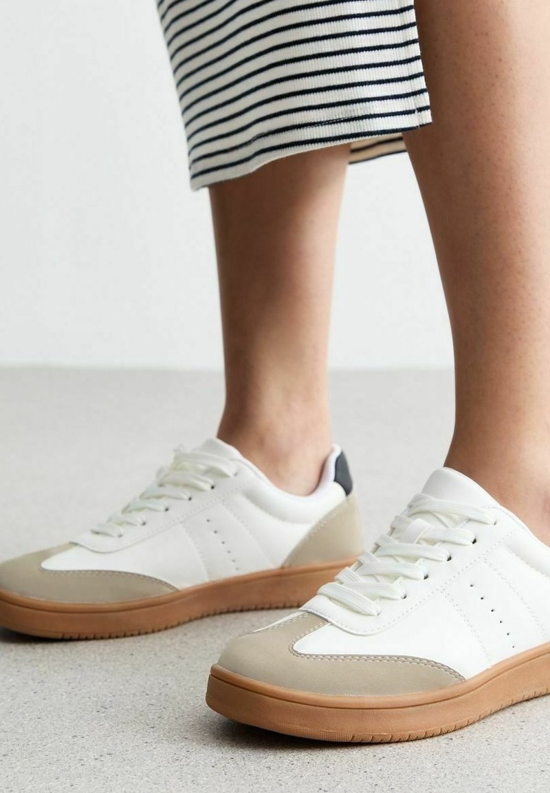 Vita sneakers med beige detaljer, gummisula och snörningsdesign. Har perforerad sidodetalj och svart häldrag.