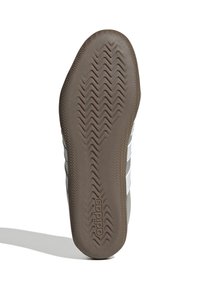 Sole della scarpa in gomma marrone con motivo di trazione a zigzag, caratterizzata da lati grigi e tre strisce bianche; include un logo vicino al tallone.