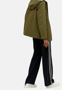 Olijfgroen gewatteerde jas met een relaxed fit, gecombineerd met zwarte wijde broek met witte zijkanten en witte sneakers.