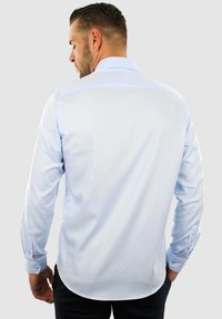 Lichtblauwe langärmige shirt met een soepele textuur, smal ontwerp en een gebogen zoom. Voorzien van knoopmanchetten en een klassieke kraag.