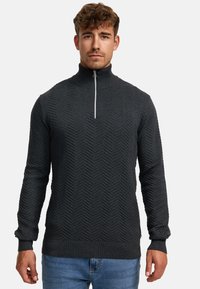 Dunkelgrauer Strickpullover mit hohem Kragen, der ein Fischgrätenmuster aufweist und einen halblangen Reißverschluss hat. Rippbündchen und Saum vervollständigen das Design.