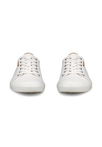 Par de zapatillas blancas de corte bajo con cordones blancos, punteras redondas y pequeños parches de logo color canela cerca del tobillo sobre un fondo blanco.