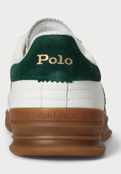 Sapatilha de couro branca com aba de calcanhar em camurça verde, apresentando o logótipo dourado "Polo" e sola de borracha castanha com "Ralph Lauren" em relevo.