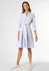 Blau-weiß gestreiftes Hemdkleid mit 3/4-Ärmeln, Knopfleiste, Taillengürtel und ausgestelltem Rock, kombiniert mit weißen Sneakers.