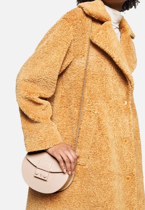 Pomarańczowy płaszcz z teksturą i kołnierzem, z dużymi guzikami oraz kremowy top. Beżowa okrągła torebka z klapką i łańcuszkowym paskiem.