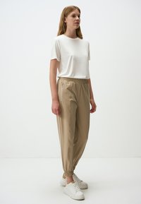 Witte t-shirt met korte mouwen gecombineerd met beige elastische broek met ritszakken, een gladde textuur en elastische boorden. Witte sneakers.