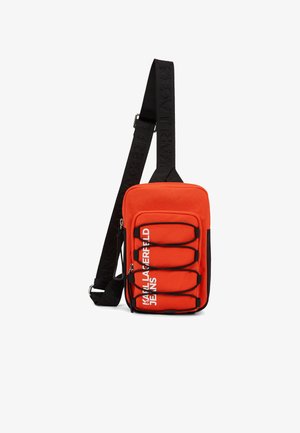 Kompaktne punane õlakott musta reguleeritava rihmaga, ees elastsete nööridega ning valge "KARL LAGERFELD JEANS" tekstiga taskul.