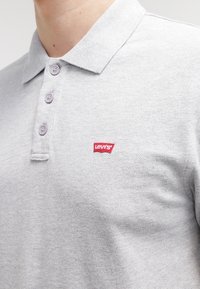 Polo grigio chiaro realizzato in tessuto testurizzato. Presenta una chiusura con tre bottoni e un piccolo logo rosso di Levi's sul petto.