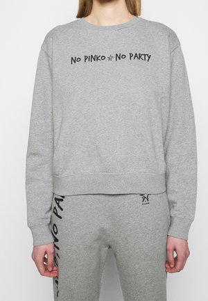 Osoba nosząca szarą bluzę i pasujące spodnie dresowe z czarnym napisem "No PINKO No PARTY" na obu.