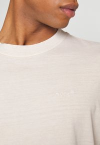 Beżowa bawełniana koszulka z okrągłym dekoltem i haftowanym logo "Levi's" w tonacji kolorystycznej. Gładka tekstura i prosty design.