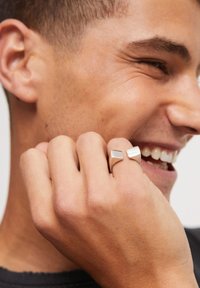 Bagues géométriques en argent sur une main, présentant une finition lisse et polie. Les bagues ont des formes rectangulaires et sont portées sur deux doigts.