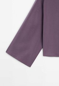 Haut en tissu violet léger avec un design à manches larges et amples ; texture lisse ; aucun motif ni détail matériel visible.