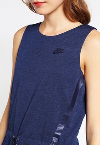 Navy blue athletic tank top with a smooth texture and a round neckline. Features a black Nike logo and sleek side satin accents.