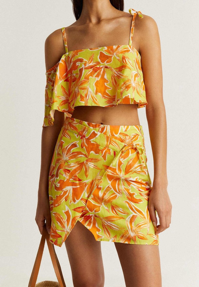 Ensemble crop top et jupe enveloppante en jaune avec imprimé floral orange. Comprend des bretelles fines, un ourlet volanté et un accent à nouer sur la jupe.