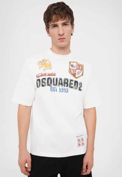 T-shirt blanc à manches courtes présentant des graphiques multicolores, incluant un lion, des boucliers et du texte, fabriqué en coton avec une coupe décontractée.