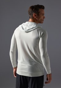 Camisola com capuz de mangas longas em cinza claro, feita de tecido texturizado; apresenta um design ajustado e punhos em malha. Sem gráficos ou padrões.