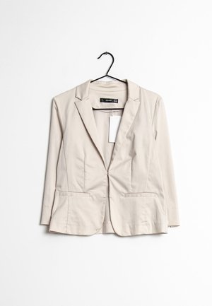 Blazer beige pour femme avec revers à cran et poches avant, accroché sur un cintre noir sur fond blanc.