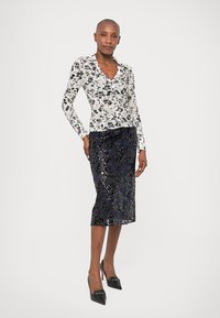 Blúzka s dlhým rukávom v čierno-bielom kvetinovom vzore, spárovaná s priliehavou midi sukňou z námorníckej modrej s flitrami a čiernymi lodičkami s ostrou špičkou.